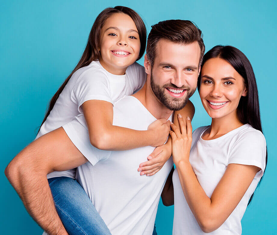 family of 3 smiling with dad with daughter on back.